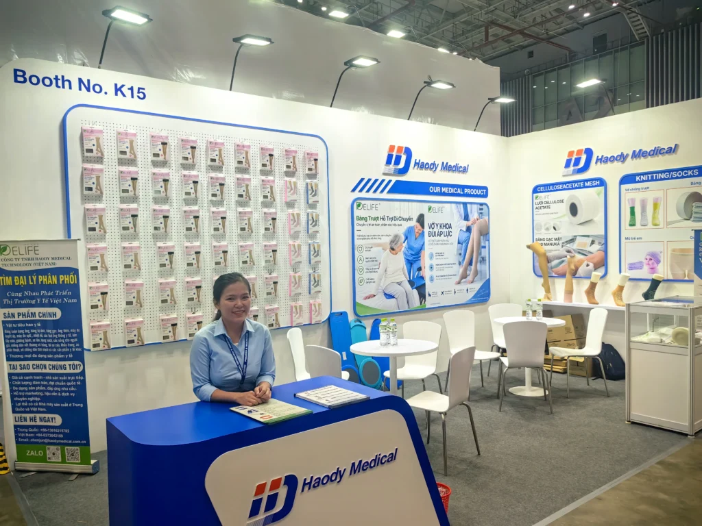 Haody Medical Booth K15 with a team member, packaged hosiery and medical product displays at PHARMEDI Vietnam 2026